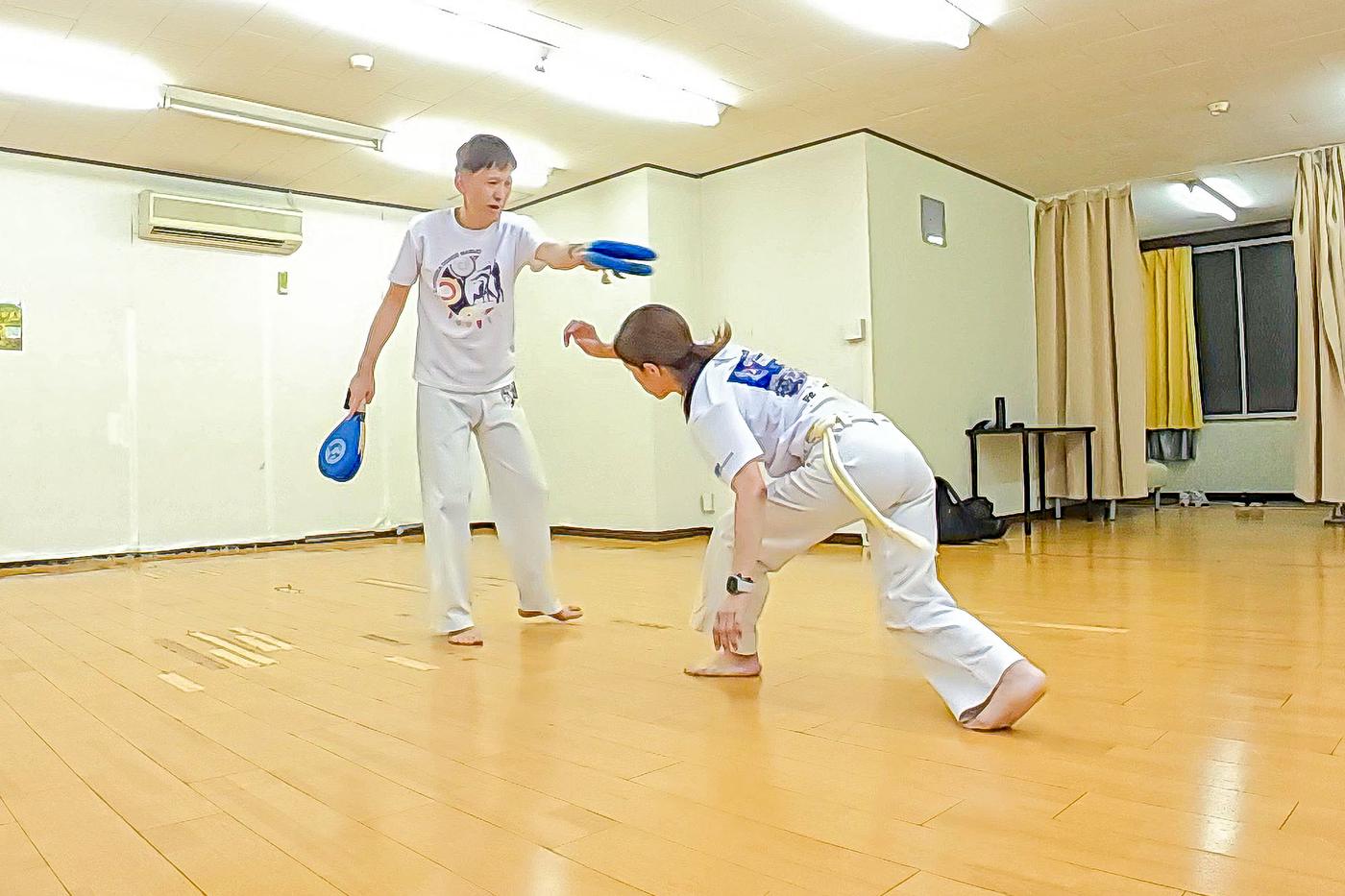 教室の会場で二人一組になり、一方が構えた的に向けてもう一方が蹴る練習をしている様子